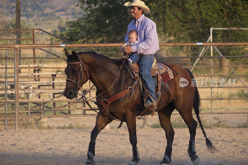 年轻的西方父亲抱着他的女儿在他的腿上，他骑着他的马绕着竞技场散步。