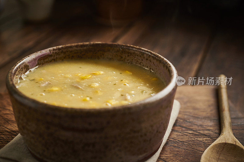 古色古香的木头桌面上放着一只质朴的碗，里面盛着鸡肉和甜玉米汤。