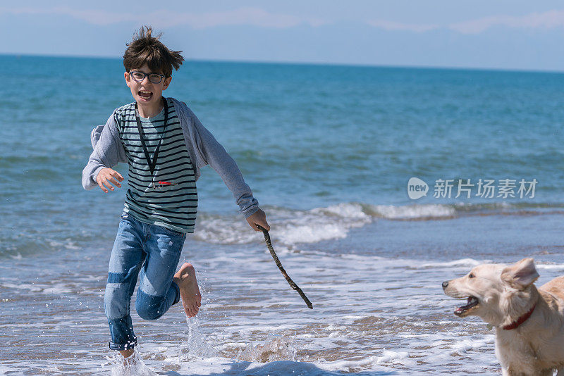 快乐的男孩和她的狗在沙滩上奔跑。