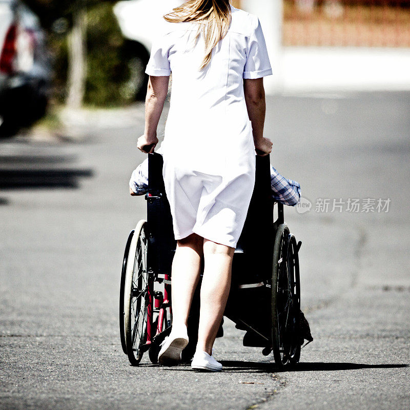 年轻护士推着病人穿过停车场的背影