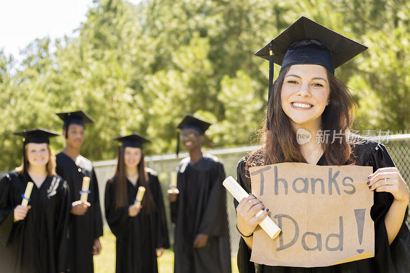 教育:拉丁女孩毕业后举着“谢谢爸爸”的牌子。朋友。