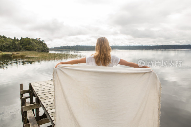 女人站在湖码头上，拿着毯子在空中
