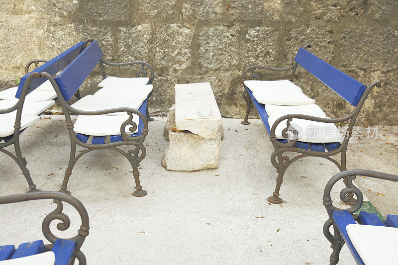 混凝土地板上有几张蓝色的空长凳，靠在历史悠久的墙上