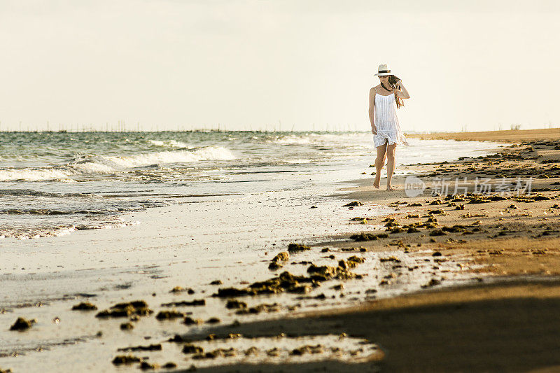 美丽的女人走在讨厌的海滩与白色的裙子