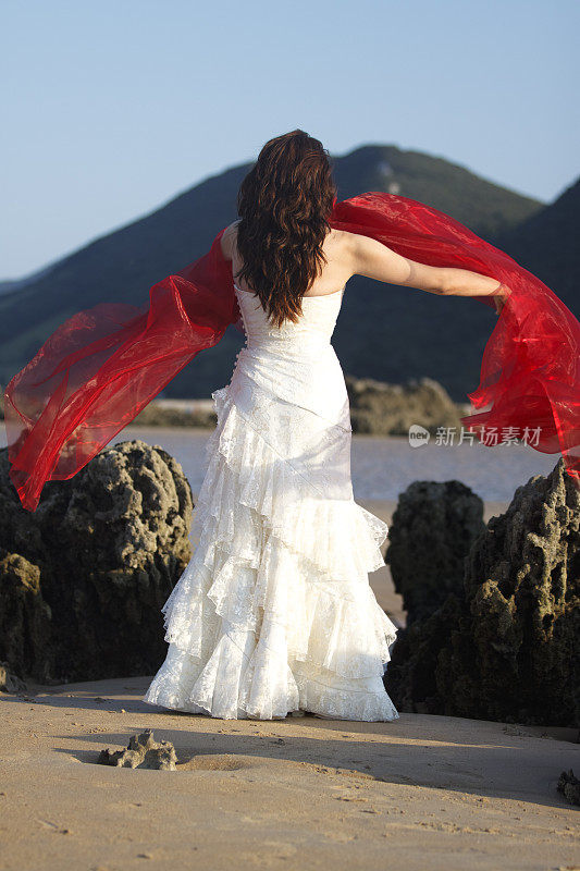 新娘穿着红色薄纱在海滩上散步