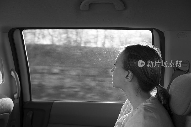 在高速公路上，后座上的年轻女子望着窗外