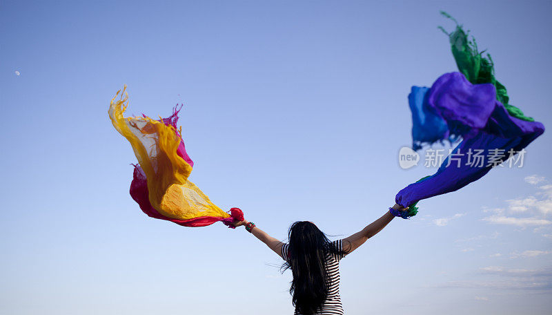 一个年轻女人拿着五颜六色的披肩在天空中