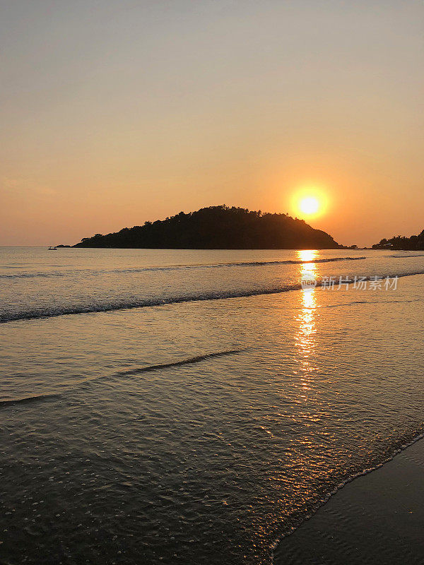 图像的日落在果阿海滩海在冬季日落，Palolem，南果阿，印度，度假，橙色的日落倒影照片，拍打的海浪在热带海岸和海岸线上的棕榈树在背景