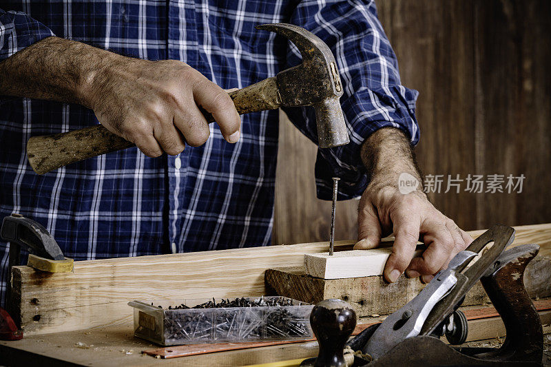 成熟的木匠使用锤子和钉子在家庭车间木板的特写