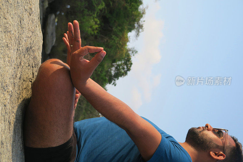 印度男子练习莲花姿势(莲花瑜伽)瑜伽位置在岩石，水的边缘，帕洛伦海滩，果阿，印度