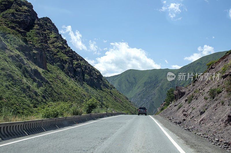 汽车在风景如画的青山之间的道路上行驶。旅行在吉尔吉斯斯坦