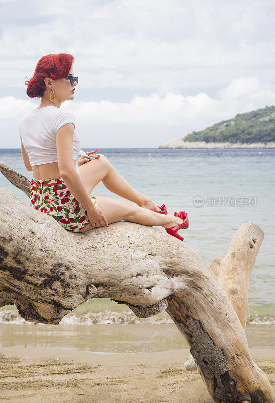 美丽的女孩坐在海滩上的一根旧圆木上