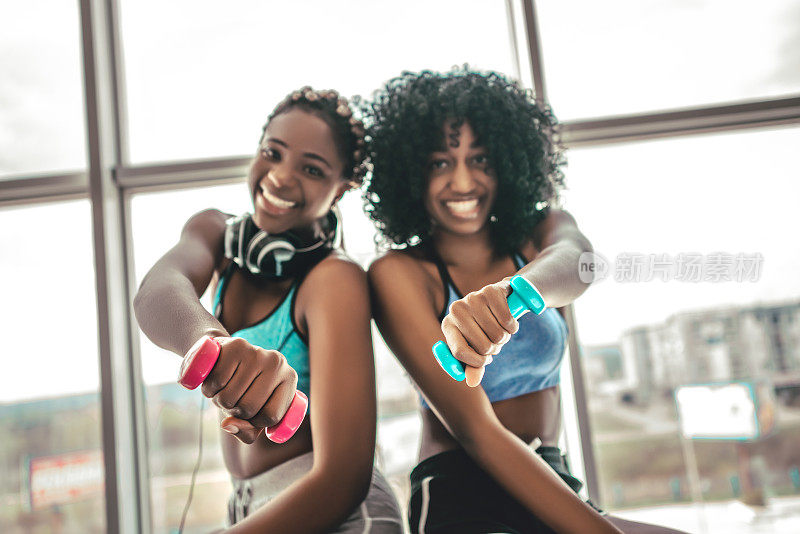 快乐健康的年轻非裔美国女人在健身房用一对哑铃锻炼