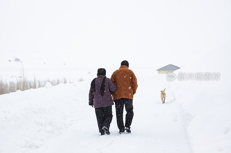 一对老年夫妇在下雪的乡村路上穿着暖和的衣服