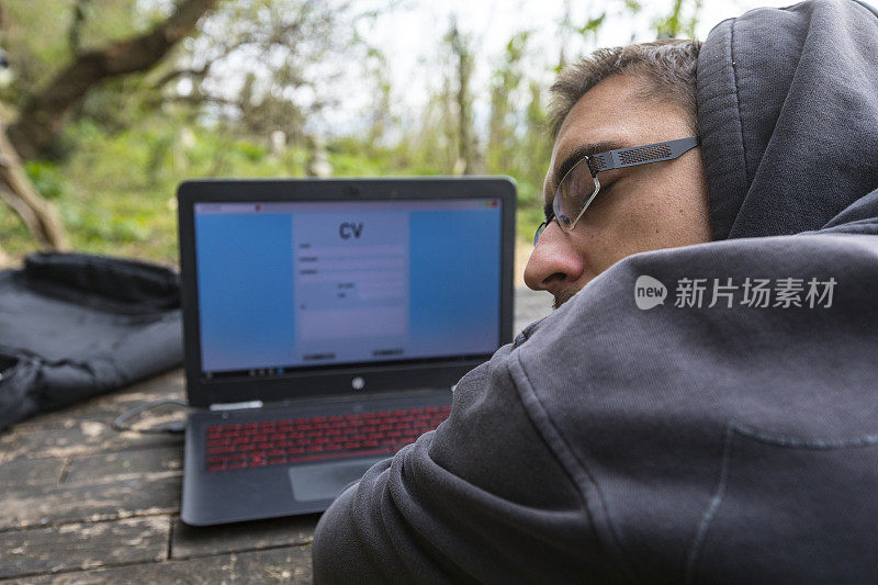 疲惫的失业青年坐在自然中，电脑显示器上放着在线简历