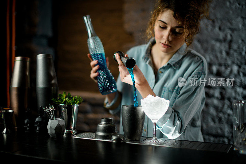 职业女调酒师将蓝色饮料从jigger倒入杯子。