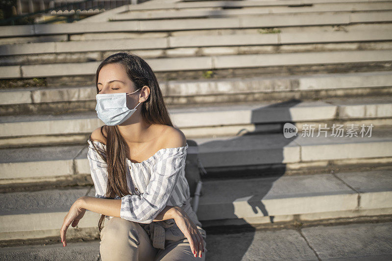 冠状病毒大流行期间戴医用口罩坐在楼梯上的妇女肖像