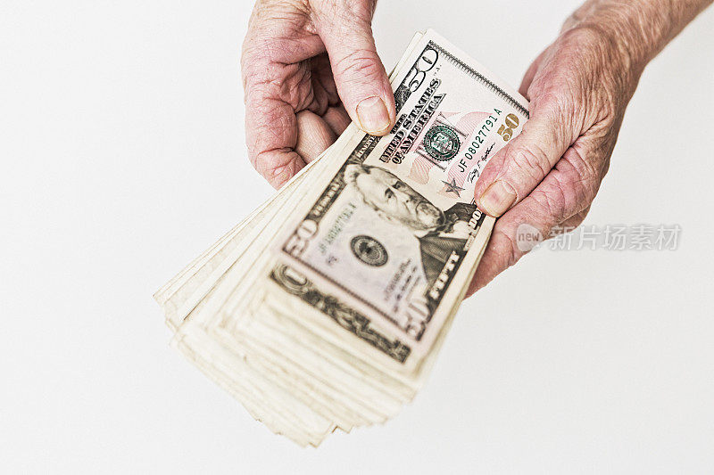 老妇人布满皱纹的手里拿着一叠现金，上面有一张50美元的钞票