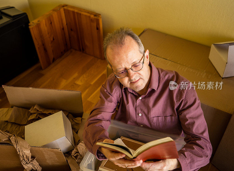 一个中年白人男子在空荡荡的公寓房间里读着一本旧日记，从纸箱里取出行李准备搬家