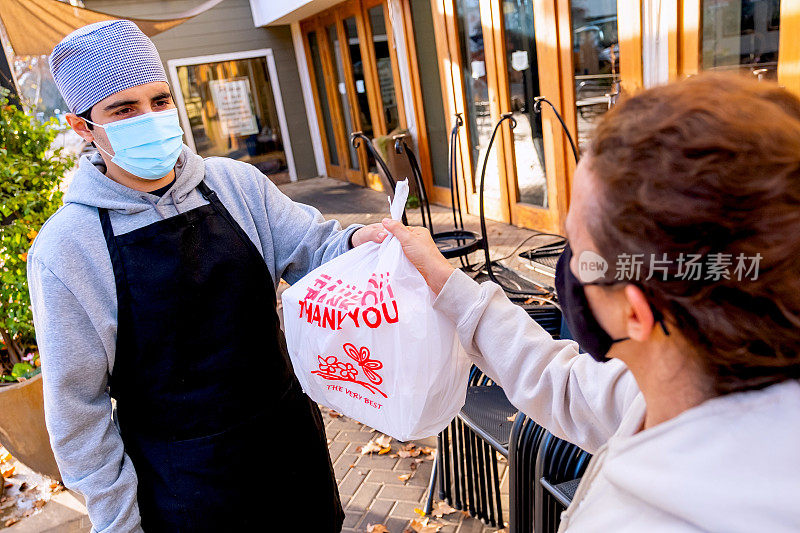 一名女子在路边的小货车上取餐，两人都戴着防护口罩