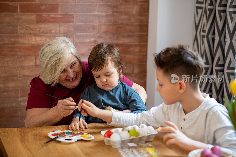 小孩坐在奶奶的腿上。他们正在用画笔和蛋彩画彩蛋。