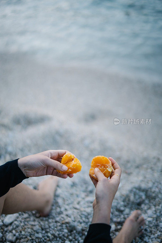 年轻女子在岩石海滩上吃橘子当早餐