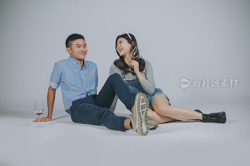 一对亚洲华人夫妇坐在地上用酒杯拍摄，工作室用灰色背景剪出来