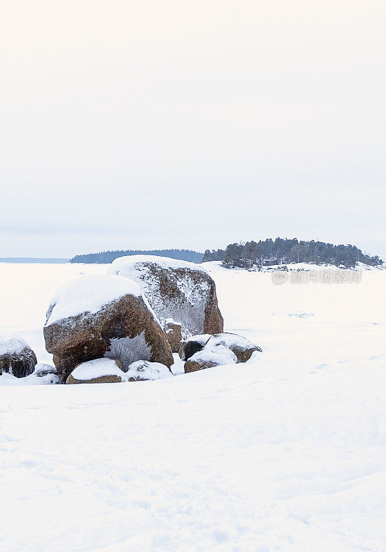 冬天的风景。这是一块巨大的花岗岩，背景是冰雪覆盖的海湾。地平线上的一个岛屿。