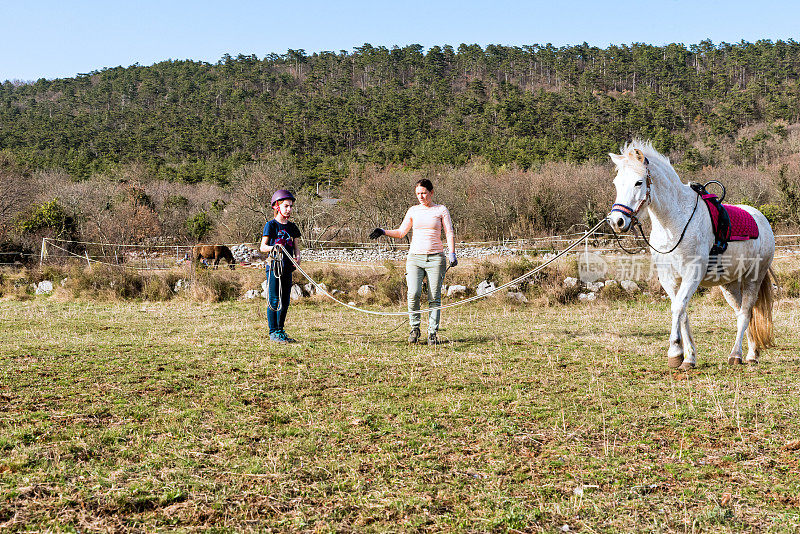 年轻的女孩与教练训练骑马在牧场与白色威尔士小马在冬天