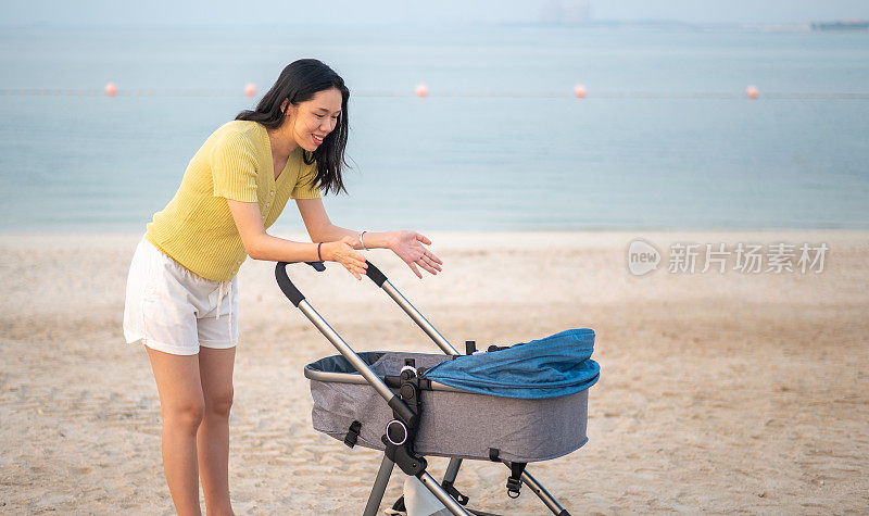 日落时分，母亲抱着一辆婴儿车在海边的沙滩上