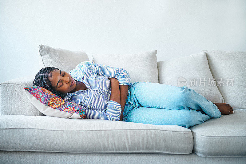 一名年轻女子躺在家里的沙发上，肚子痛
