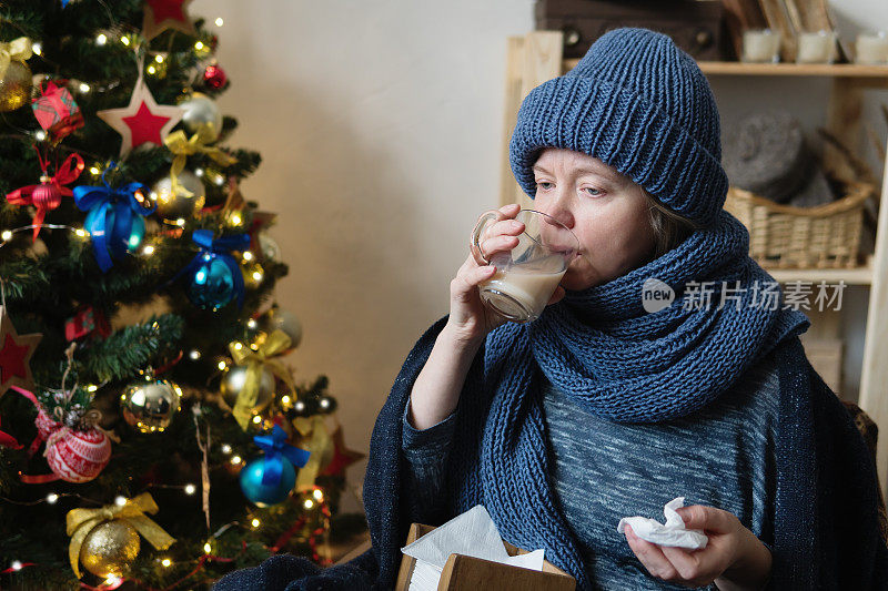 生病的女人，裹着毯子，拿着一杯热饮。
