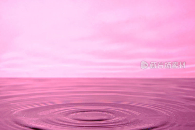 明亮的粉红色背景与发散的圆圈从水滴表面的水。