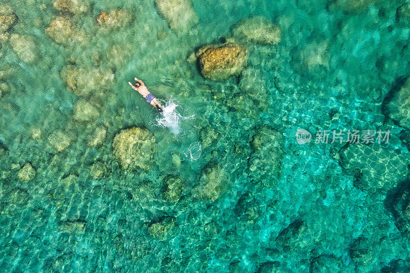 航拍的一对年轻夫妇浮潜在珊瑚礁上，到达了更深处清澈的海水，罗德岛，希腊。无人机拍摄的一对情侣浮潜在清澈的水中游泳。