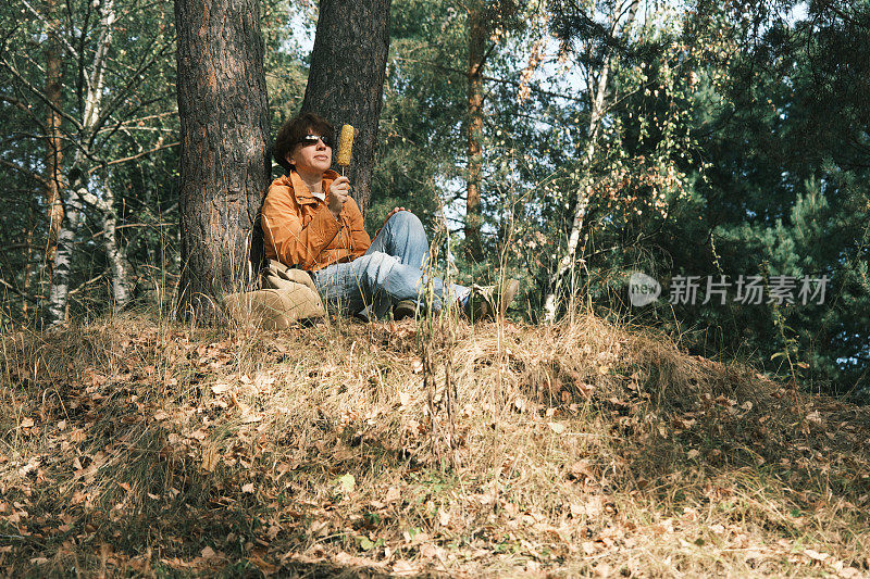 开朗成熟的女人在秋天的自然公园休息时享受烤玉米