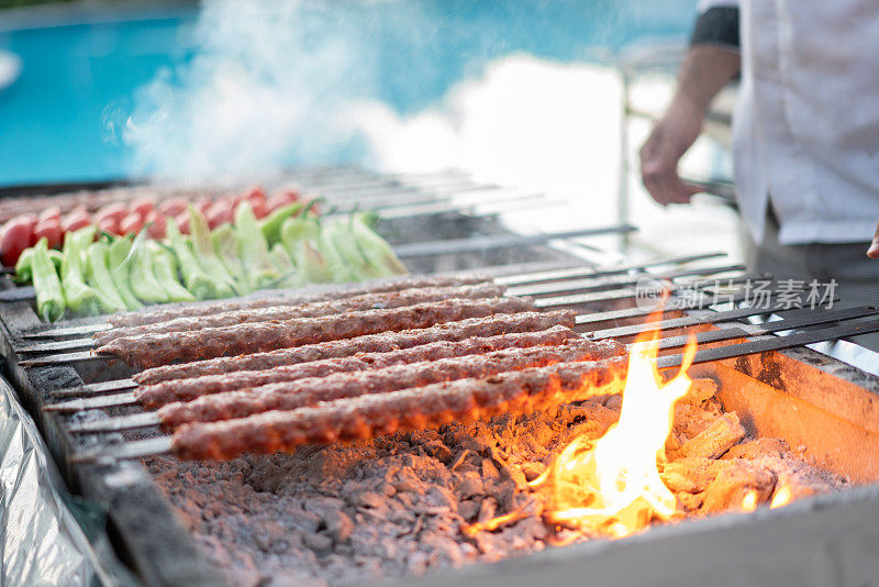 厨师在度假村游泳池附近的火焰上做烤肉串