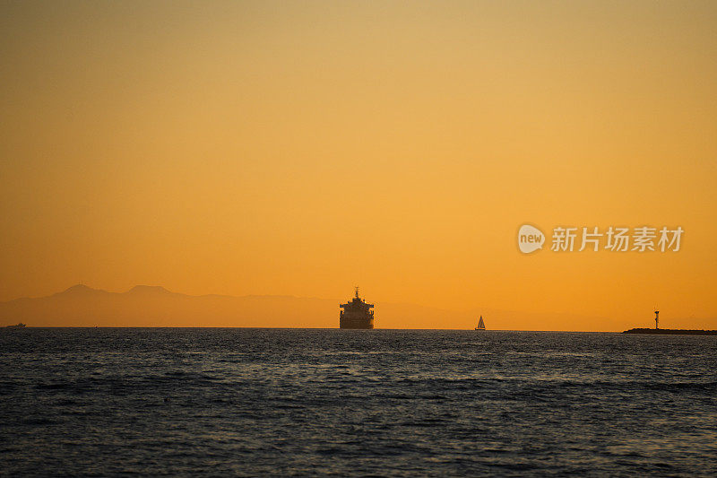 平静海面上的工业集装箱或油轮与一艘帆船在太平洋洛杉矶附近美丽清晰的日落上接近