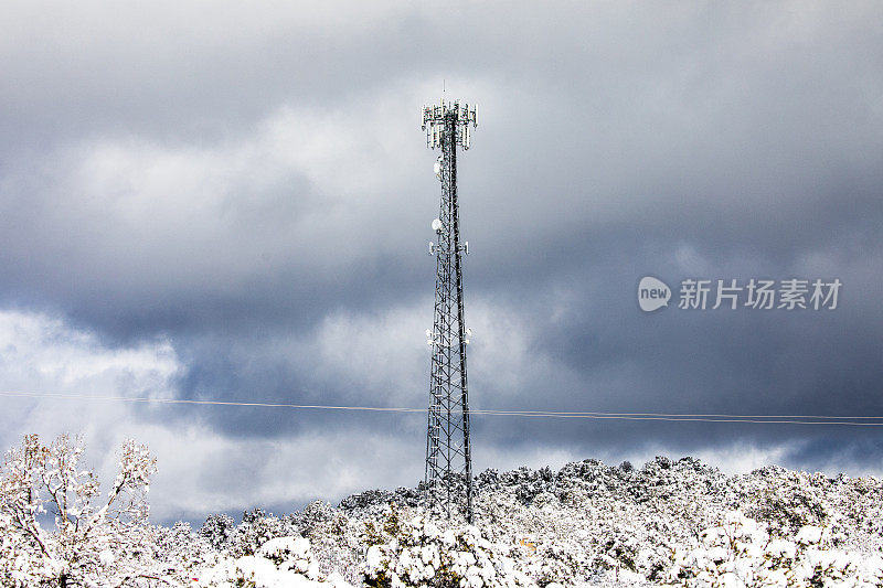 5G蜂窝通信塔周围是白雪覆盖的树木，背景是戏剧性的天空