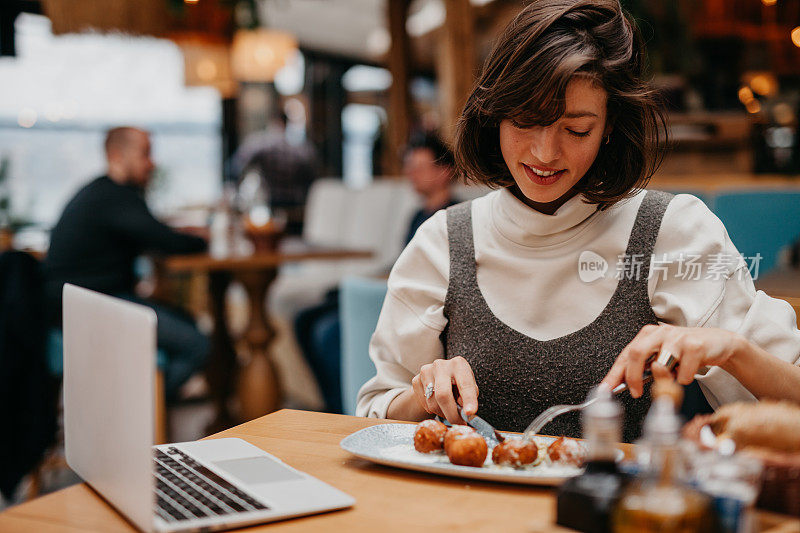 一位优雅的女士在餐厅里独自享用商务午餐，同时在笔记本电脑上工作，这说明了高效工作的概念。