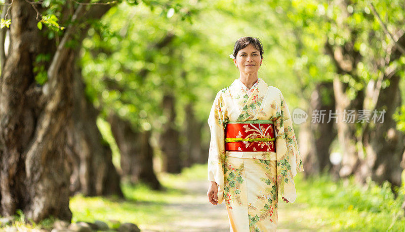 一位穿着和服的日本女游客走在一条有树的小路上