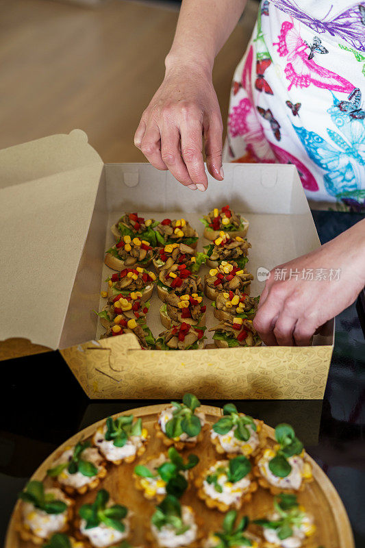 一位女厨师正在准备新的食物订单，并把它们装进盒子里。