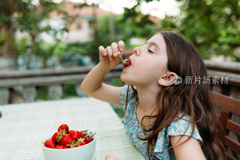 小女孩坐在桌边，吃着新鲜采摘的草莓