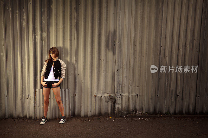 在黑暗的城市背景下，年轻女性站在钢墙前