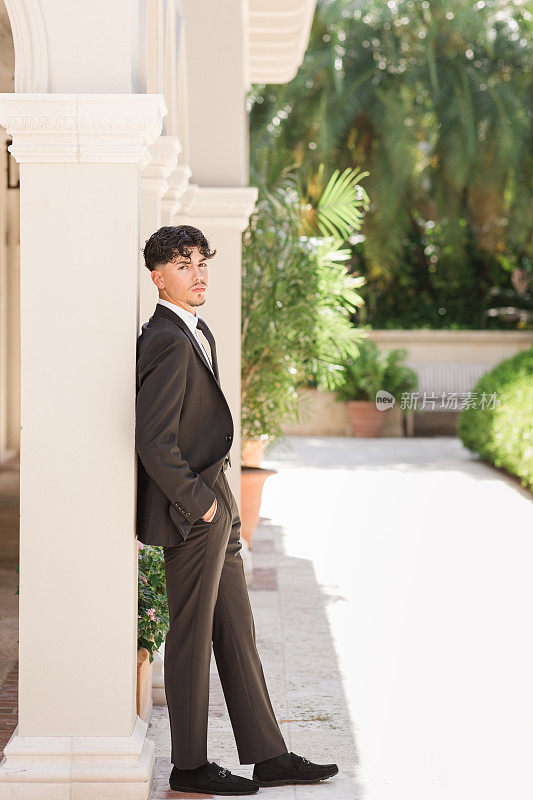 一位18岁的古巴裔美国人，穿着一身黑色西装，白色衬衫，黑色领带和黑色麂皮鞋，棕色头发和棕色眼睛，穿着西装和领带，在佛罗里达州棕榈滩的一个优雅的地方看起来清新而敏锐