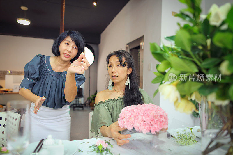 一位亚洲美丽的花艺女老师目前正在教花艺学生如何安排花艺材料，创造美丽的花艺作品。