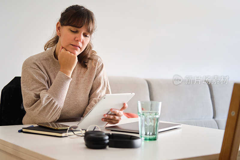 一个年轻女性在家里用数码平板电脑仔细阅读的中镜头肖像