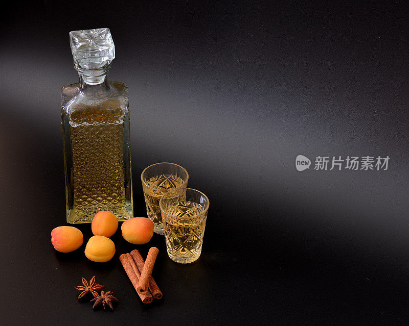 杏味利口酒与香料在黑色背景下，浓重的自制酒精在一个酒瓶和两个杯子中，成熟的水果，茴香和肉桂。