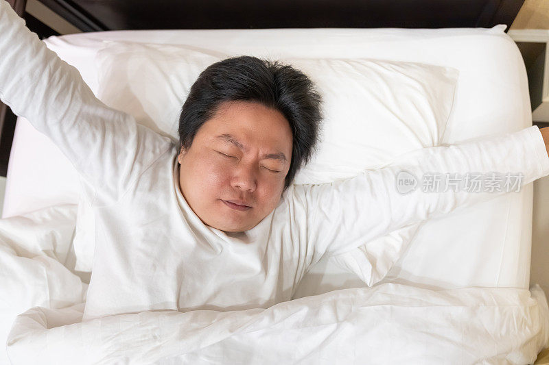 亚洲男人在床上舒舒服服地伸伸懒腰，开始一天的生活，感觉精力充沛、心满意足。