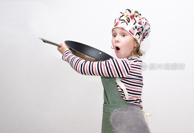 一个8岁的白人女孩打扮成厨师，手里拿着一只大煎锅，挥舞着它，开心地笑着。