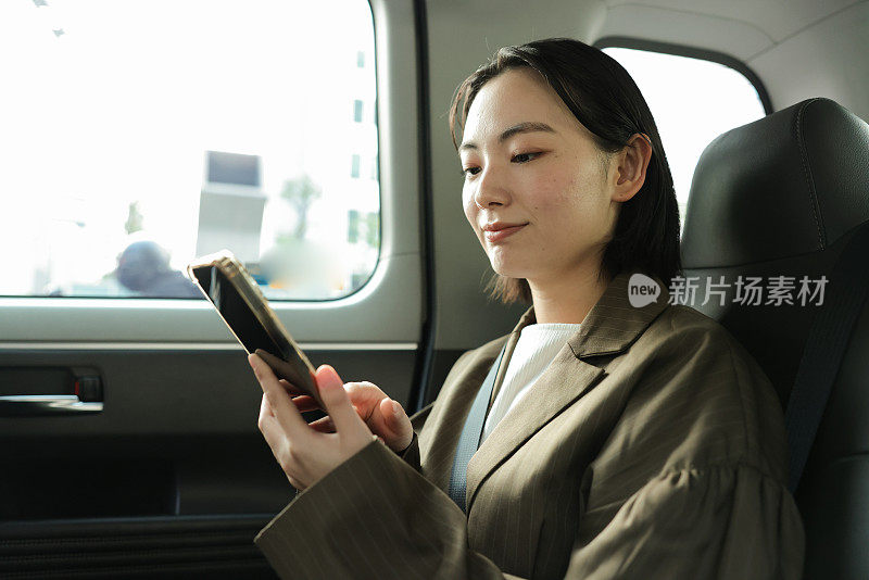 亚洲女商人乘出租车旅行时使用手机